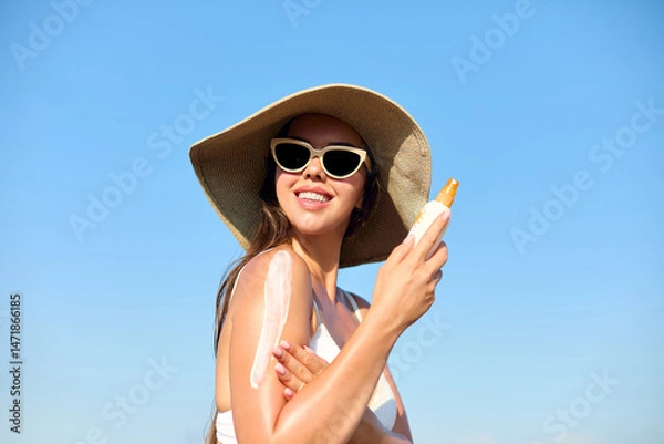 Fototapeta Woman applying sunscreen creme on tanned shoulder. Skincare Concept.  Body Sun protection suncream. Gir applying moisturizing sunscreen lotion on back.