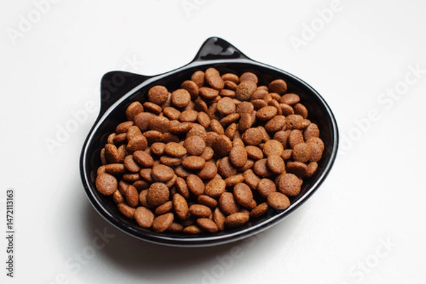 Fototapeta Dry food in black ceramic bowl in shape of cat with ears, isolated on white background.