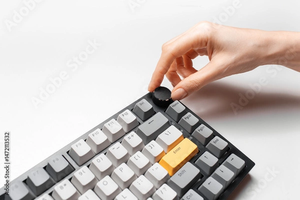 Fototapeta Female hand adjusting volume control on keyboard with yellow and grey key cap, on white background.