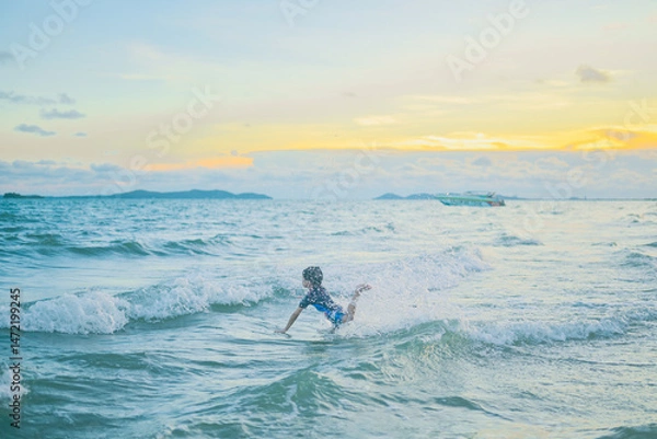 Fototapeta Joyful Ocean Plunge: A young child splashes and plays joyfully in the ocean waves at sunset, embracing the vibrant hues of the sky and the refreshing spray of the water.