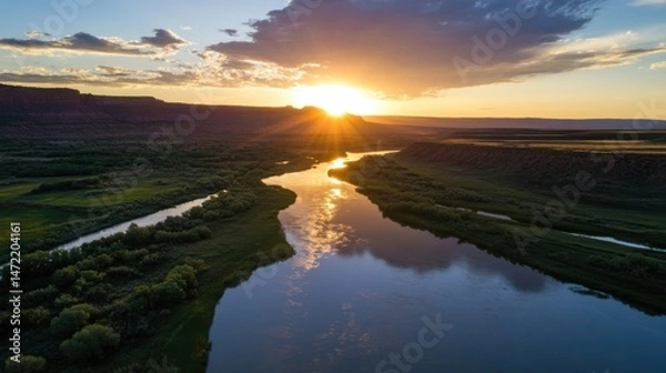 Fototapeta Sunset over a meandering river in a canyon landscape, reflecting golden light on calm water, surrounded by lush green vegetation and red rock formations. : Generative AI