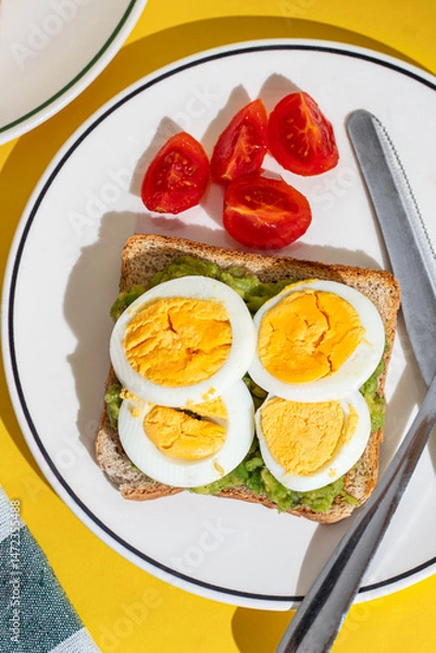 Obraz Plate of toast with boiled eggs and avocado served on a plate on yellow background