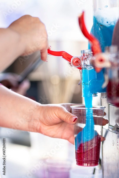 Fototapeta Filling plastic cup with colorful sirup crushed fruit ice. Frozen mixed blue and red refreshing summer drink. Refreshing Granitas