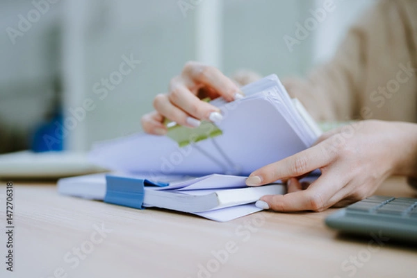 Obraz Hands of businessman hold pen for work in stacks of paper files, information search for business reports and heaps of incomplete documents is achieved on a laptop computer table in a modern office
