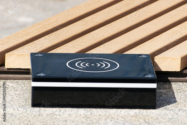 Fototapeta a device for wireless charging of electronic gadgets is installed near a bench in a city park close-up