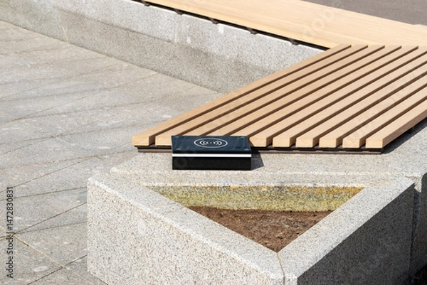 Fototapeta a device for wireless charging of electronic gadgets is installed near a bench in a city park