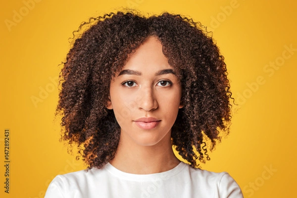 Fototapeta Human emotions and stern look of person. Serious, calm millennial african american lady with curly hair in white t-shirt looking at camera, isolated on yellow background, close up, free space