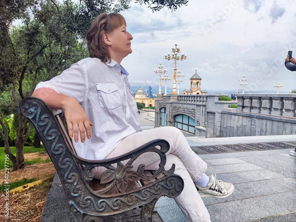 Fototapeta Mature woman enjoys a peaceful moment on a bench while exploring a scenic tourist destination during her travel adventure