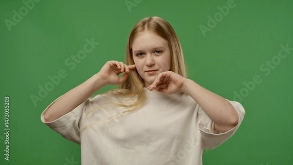 Fototapeta Teenage girl posing at camera smiling, acting like super model, positive expression, isolated on chroma key green screen studio background mockup.