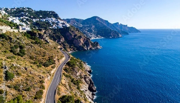 Fototapeta Coastal road winds beside the ocean beneath a hill covered with white buildings