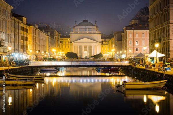 Fototapeta Trieste, Italy. Church of St. Antonio Thaumaturgo with Canal Grand in the evening. Sunset sky with boats and illuminated buildings