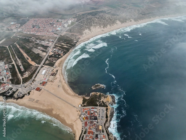 Fototapeta Wide aerial showing beach curvature, waves, and town extending inland