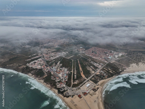 Fototapeta Wide drone shot showing inland cityscape behind beach under low clouds