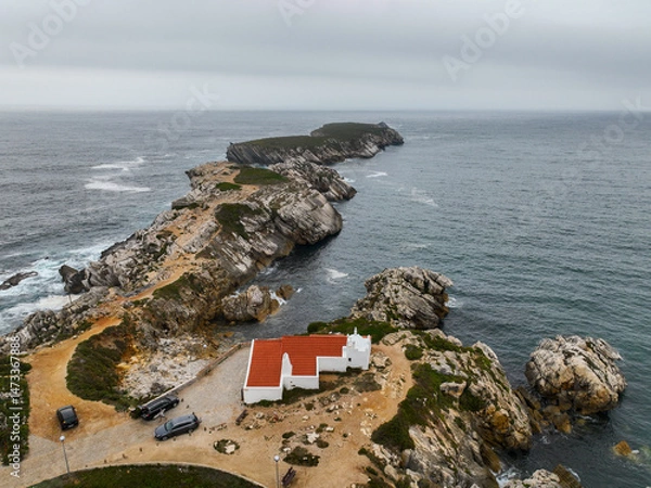 Fototapeta Drone shot of white chapel and red-tiled roof near cliffs and rocky outcrop