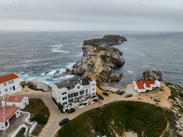Fototapeta Overhead view of white buildings and footpath leading across cliffs to islet