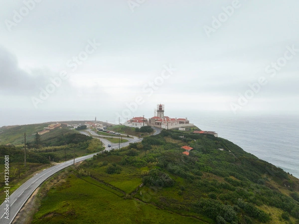 Fototapeta Distant view of winding road and red-roof lighthouse on coastal cliffs