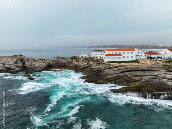 Fototapeta Oceanfront shot of rock formations with buildings above foamy waves