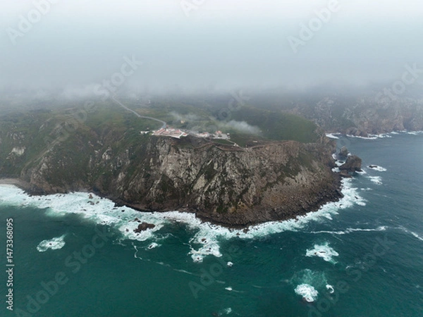 Fototapeta Wide drone image of lighthouse at edge of steep cliffs and turbulent sea