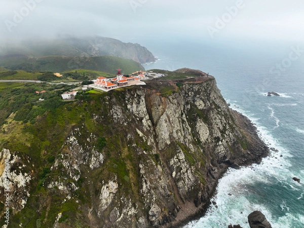 Fototapeta Drone shot showing red-roof lighthouse and jagged white cliffs above sea