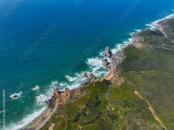 Fototapeta Aerial view of vibrant green hills descending to a rugged coastline with cliffs and rock outcrops in Portugal