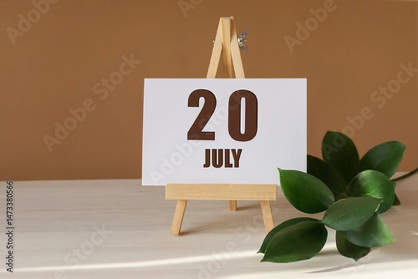 Fototapeta July 20th. Day 20 of month, Calendar date. Green branch, easel with the date and month on desktop. Close-up, brown background. Summer month, day of year concept