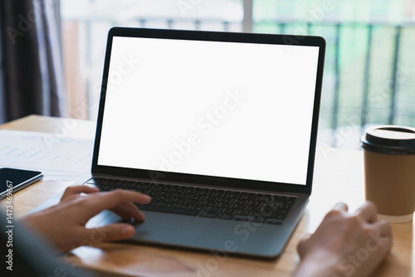 Fototapeta Businessman hand typing on laptop and working on computer on wooden table, screen blank mockup.