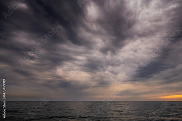 Fototapeta Sun between dark storm clouds over ocean. Dramatic seascape. Clouds and rain flurry over sea.