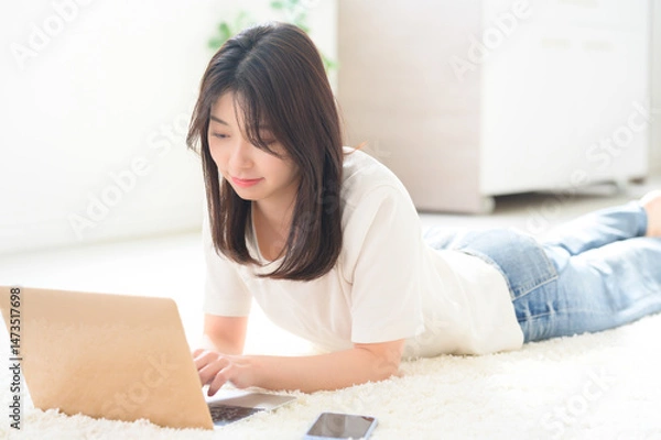 Obraz 床にうつ伏せになりながらノートパソコンに向かって作業を進める女性の自然な日常風景