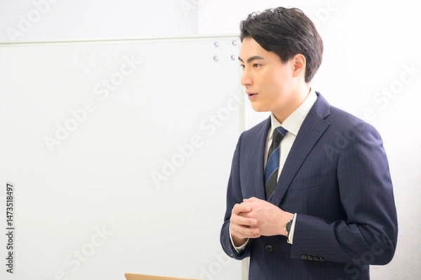 Obraz ホワイトボードの前で誠実な表情を浮かべながら話すスーツ姿の男性が伝える信頼感