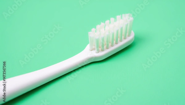 Fototapeta A toothbrush with visible bristles lies diagonally on a mint green backdrop, capturing a clean, minimalist aesthetic with realistic shadows.