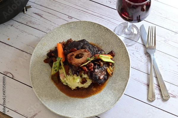 Fototapeta Plated serving of braised beef with bone in red wine sauce, accompanied by tender potatoes, root vegetables, and fresh herbs