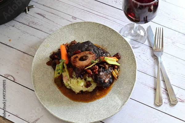 Fototapeta Plated serving of braised beef with bone in red wine sauce, accompanied by tender potatoes, root vegetables, and fresh herbs