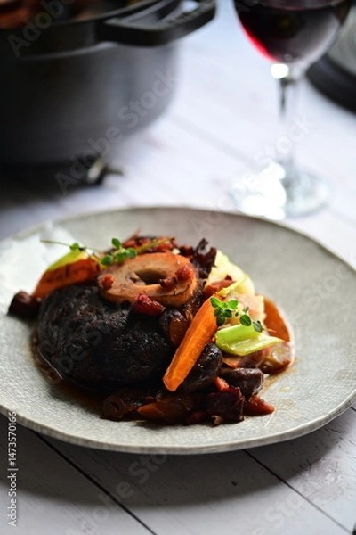 Fototapeta Plated serving of braised beef with bone in red wine sauce, accompanied by tender potatoes, root vegetables, and fresh herbs
