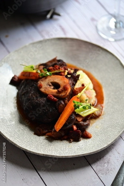 Fototapeta Plated serving of braised beef with bone in red wine sauce, accompanied by tender potatoes, root vegetables, and fresh herbs