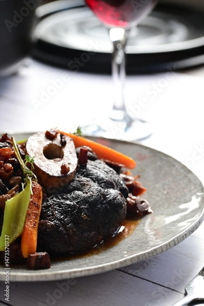 Fototapeta Plated serving of braised beef with bone in red wine sauce, accompanied by tender potatoes, root vegetables, and fresh herbs