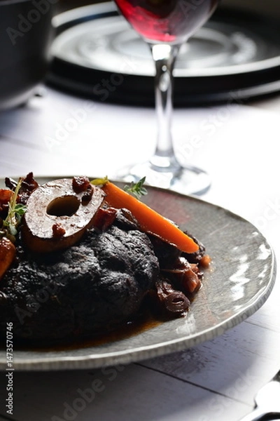 Fototapeta Plated serving of braised beef with bone in red wine sauce, accompanied by tender potatoes, root vegetables, and fresh herbs
