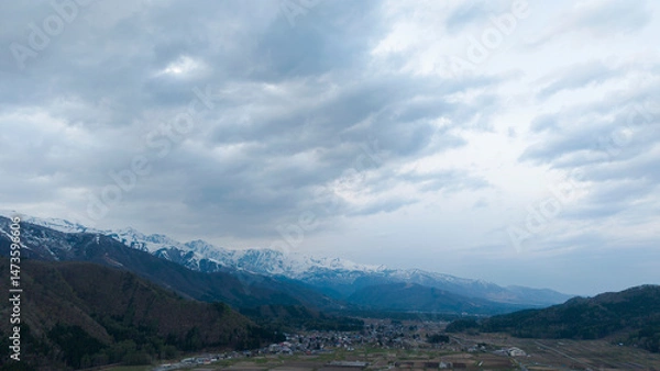 Fototapeta Landscape featuring a tranquil mountain valley with snow-capped peaks in the distance,Overcast sky A small village nestles in the valley.