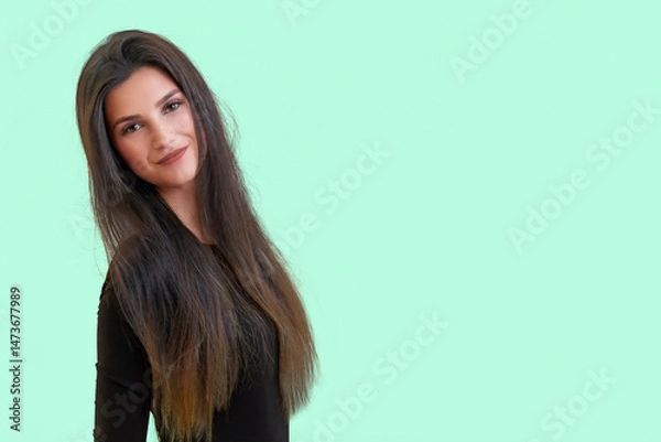 Obraz Studio waist up portrait of a tanned beautiful brunette long haired young  woman posing in front of a light green background.