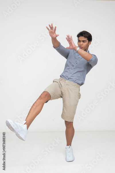 Fototapeta Southeast Asian man blown away backwards or knocked back in surprise, lifting a leg and raising hands in dramatic reaction. Isolated on a light background.