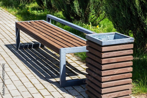 Fototapeta A beautifully crafted wooden bench that has a trash can beside it