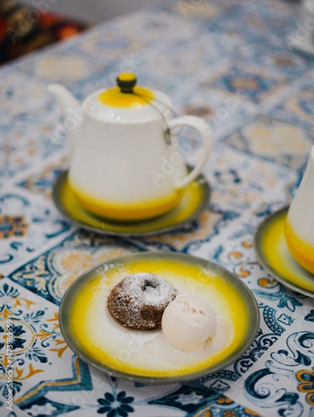 Fototapeta Chocolate cake dessert. A top view of molten chocolate lava cake icing on top  served with a scope of vanilla ice cream. Blurry teapot on the background