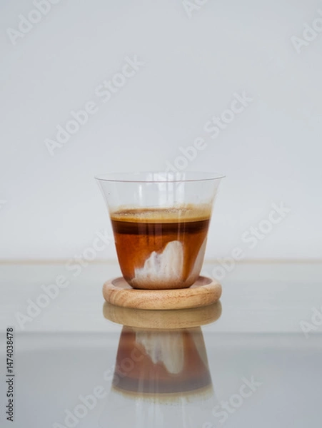 Fototapeta Dirty Coffee. A glass of specialty signature coffee called Dirty Coffee served on the wooden saucer. The refelction of coffee on the glass table and isolated on a white background.