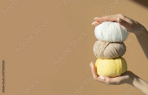 Fototapeta Stack of skeins of knitting thread are in beautiful female hands. Wool balls with yarn on a light brown background in sunlight. Mockup for advertising