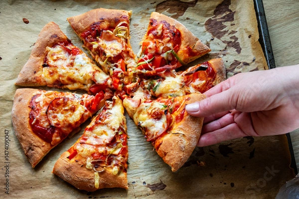 Obraz Female hand taking a slice of cut homemade pizza on baking paper. Top view
