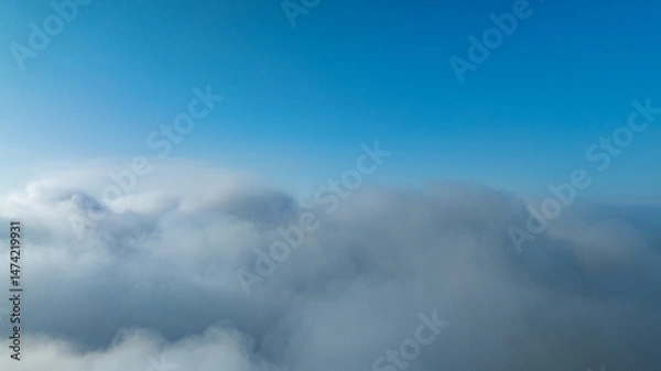 Obraz A serene view of the early morning sun rising above a vast sea of clouds, with distant mountain peaks faintly visible on the horizon, creating a peaceful and ethereal landscape. Flying over the cloud