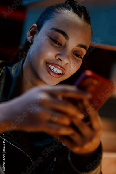 Fototapeta young woman enjoys convenience of online banking app while sitting outdoors in vibrant city at night. Female confidently manages her money transactions, staying secure and connected in digital world