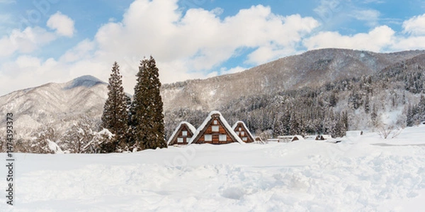 Obraz A panoramic view of three traditional gassho-zukuri houses in Shirakawa-go, Japan, surrounded by snow-covered fields and distant mountains in the background. UNESCO World Heritage 