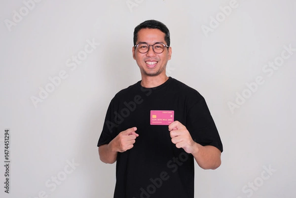 Fototapeta A man smiling confident while pointing at credit card that he hold