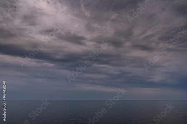 Fototapeta Sun between dark storm clouds over ocean. Dramatic seascape. Clouds and rain flurry over sea.