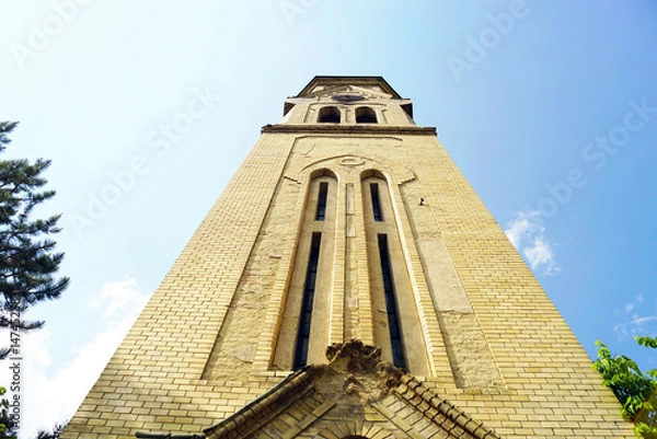 Fototapeta Photographed from the bottom up, the tall bell tower of a gothic temple built of yellow brick. Beautiful religious objects from the early 20th century in Serbia: Evangelical Church in Pancevo.